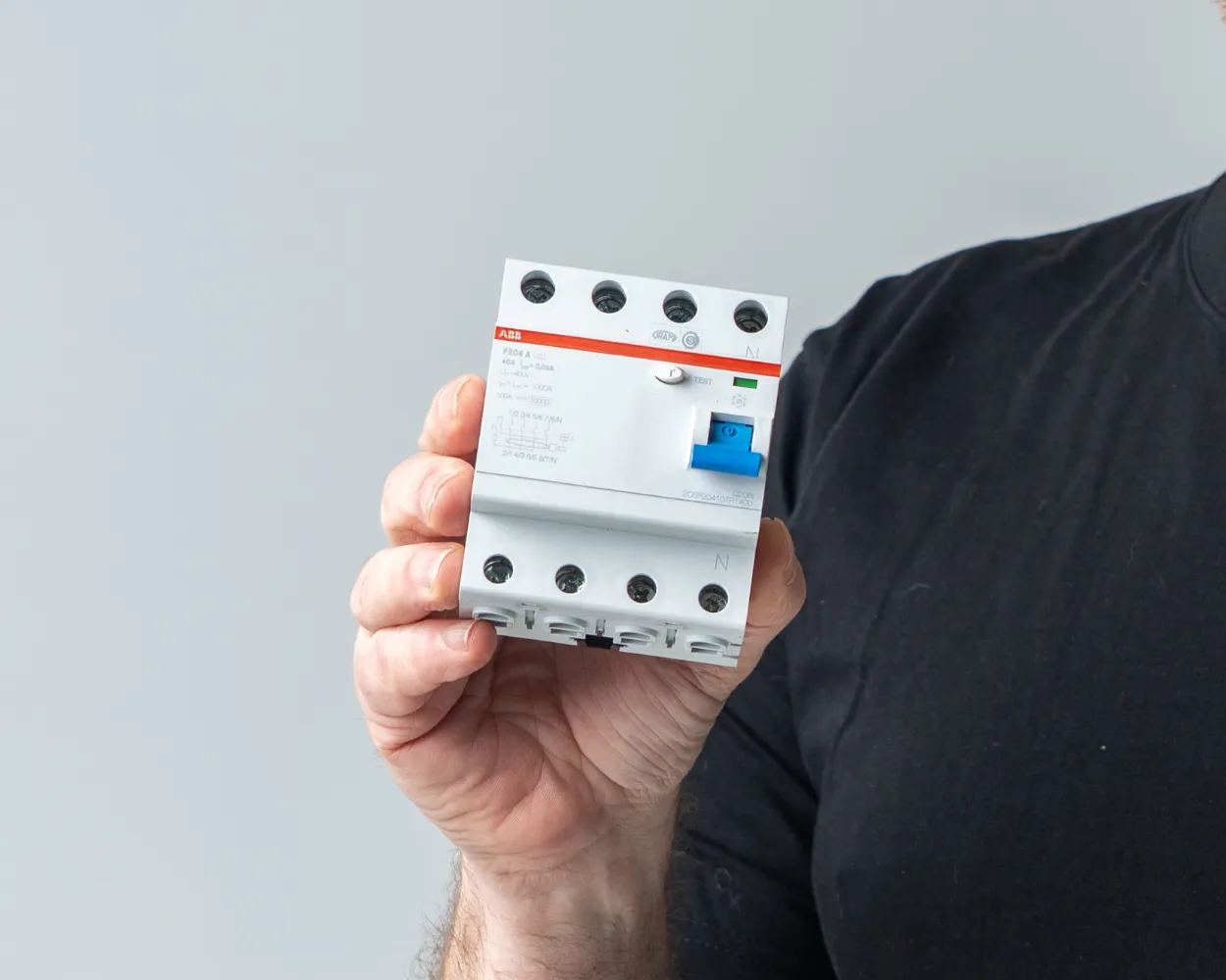 Elektricien houdt een aardlekschakelaar vast, die bij kortsluiting de stroom uitschakelt